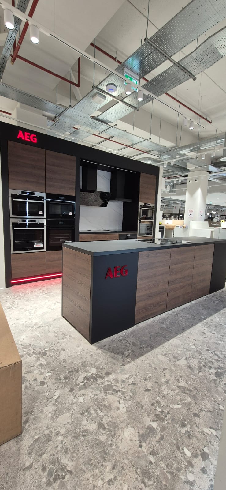 AEG kitchen display wall at Harvey Norman — dark wood veneer cabinetry with integrated ovens, hob and extraction